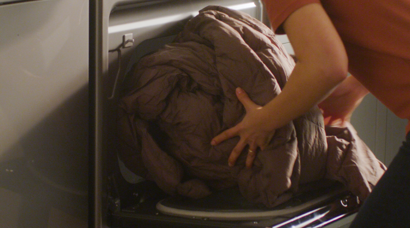 Person loading large comforter into dryer drum.
