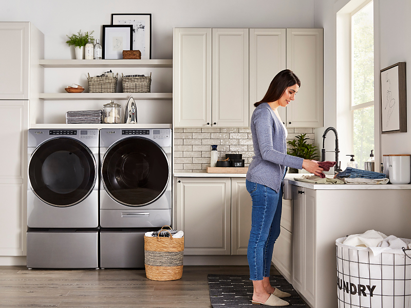 Woman in a laundry room with stainless steel Whirlpool® front load washer and dryer set