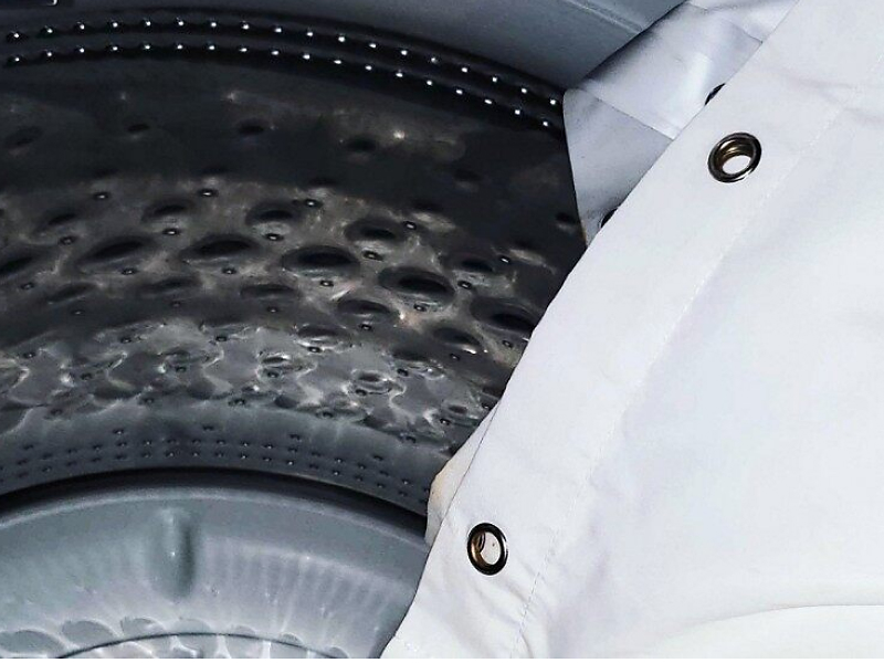 A white shower curtain being placed in a washer. A white shower curtain being placed in a washer.