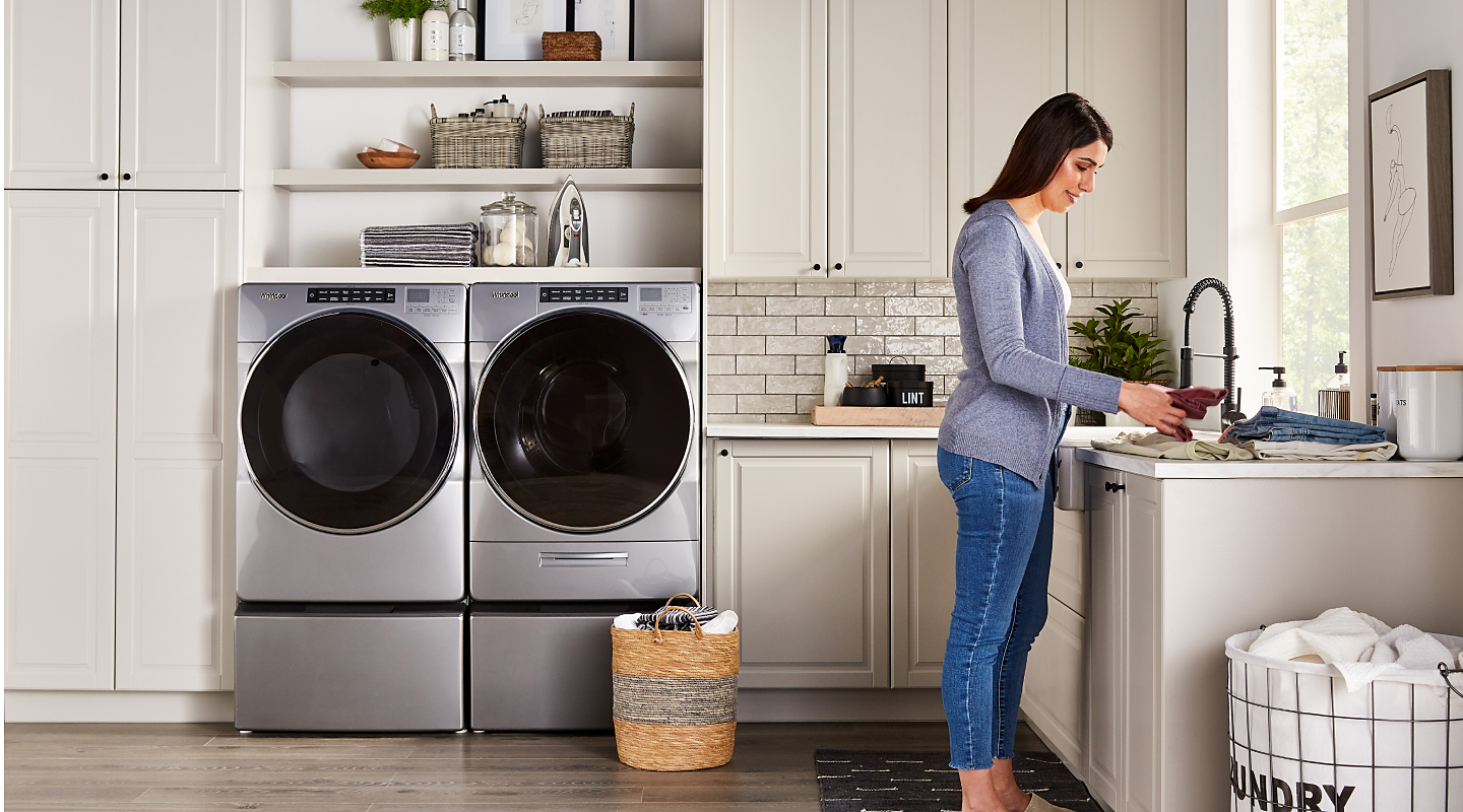 A person folding laundry with a Whirlpool® washer and dryer nearby.