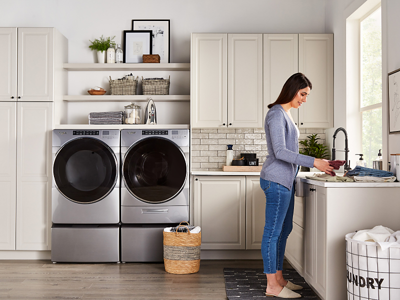 A person folding laundry with a Whirlpool® washer and dryer nearby. A person folding laundry with a Whirlpool® washer and dryer nearby.