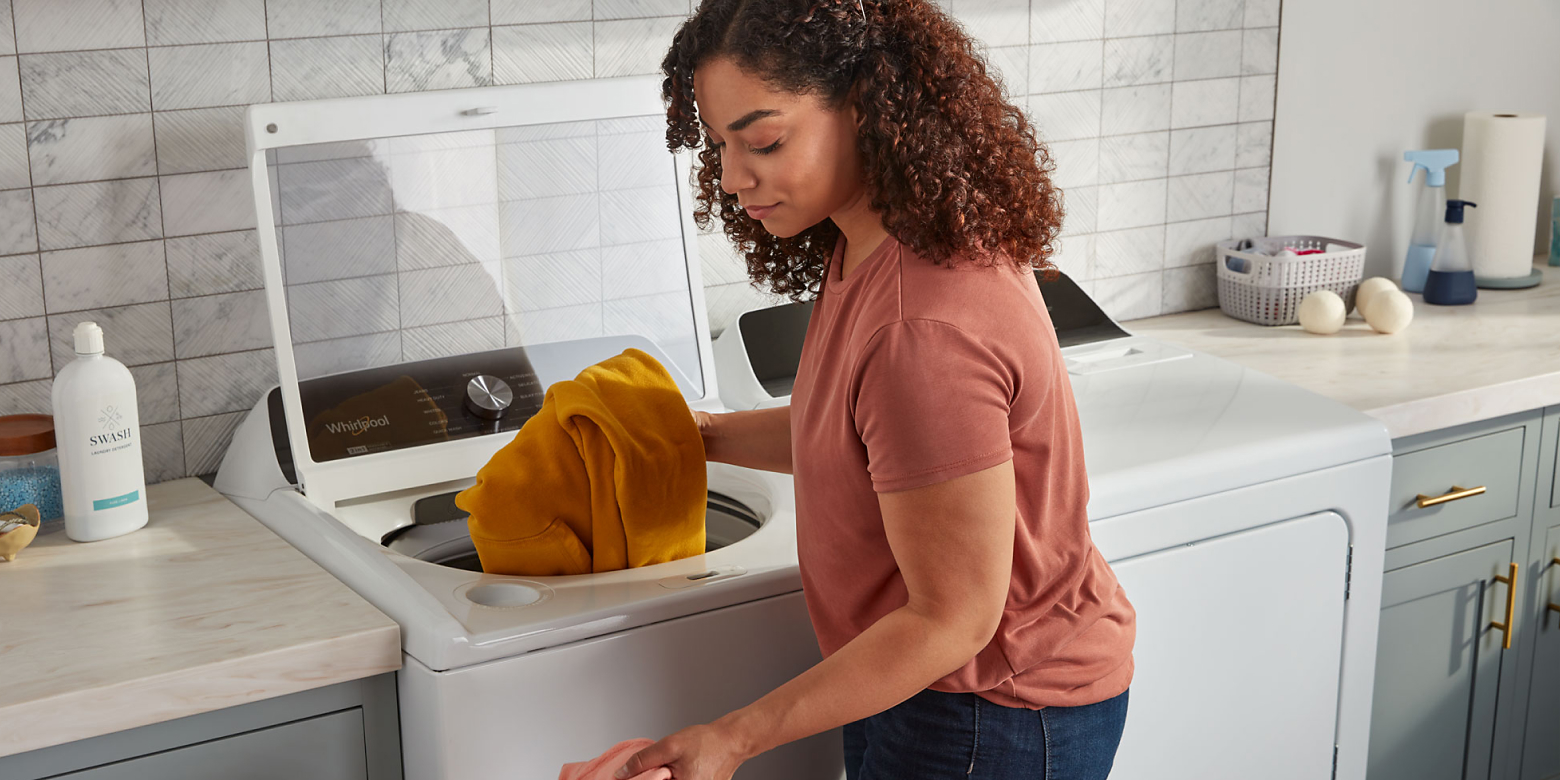 Woman loading clothes into white Whirlpool® top load washer