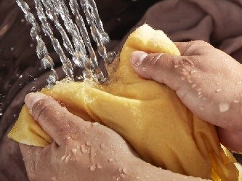 A closeup of a person adding a blanket to a Whirlpool® top load washer that’s filling with water.