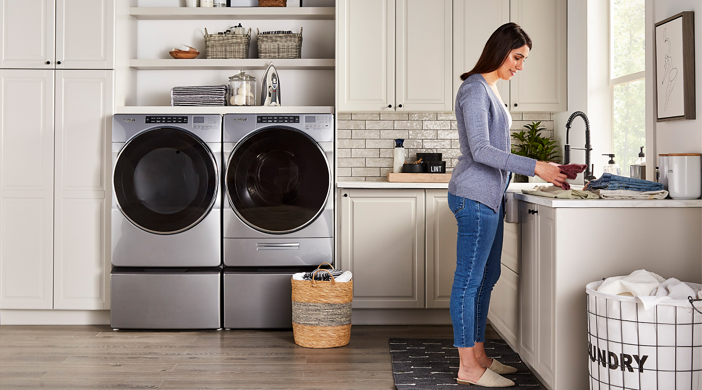 A person folding laundry with a Whirlpool® washer and dryer nearby.