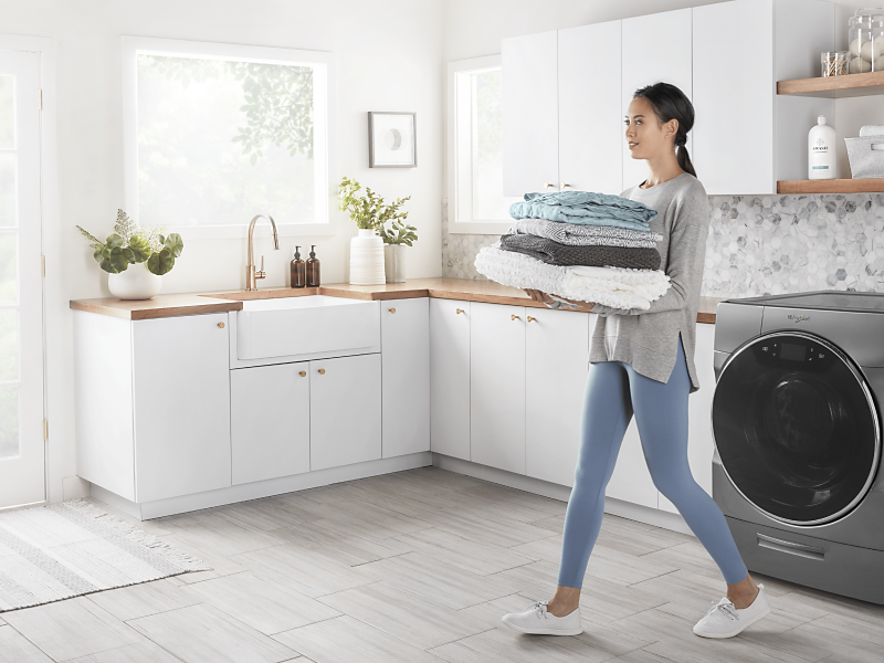 A woman carrying folded laundry cleaned by a Whirlpool® washing machine