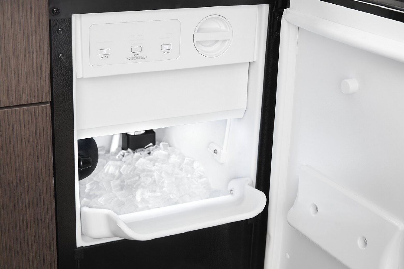 Close-up of open, standalone ice maker installed in brown cabinetry