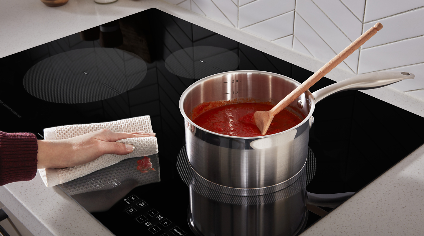 A hand wiping down pasta splatter on an induction cooktop