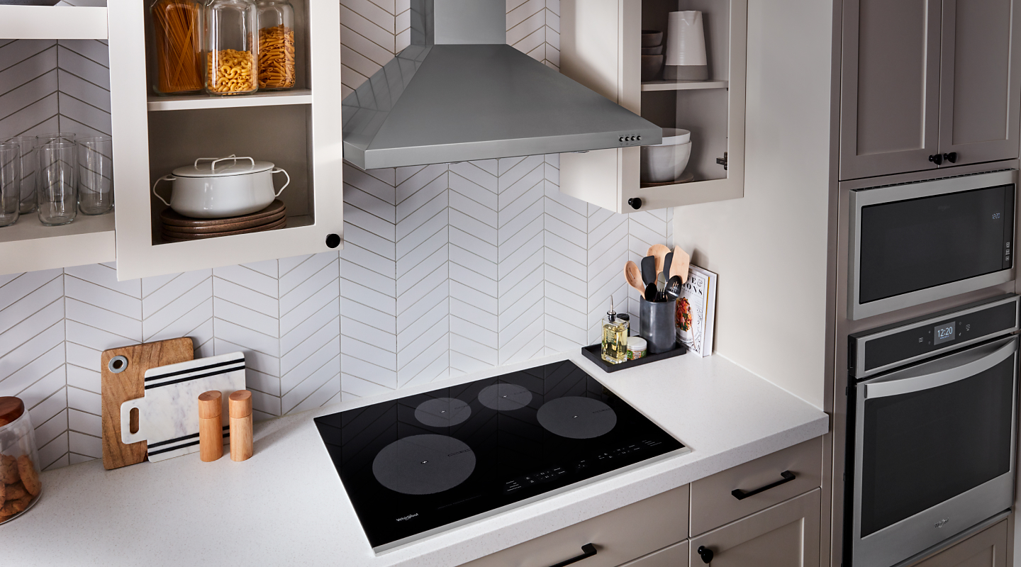 Black induction cooktop on a white counter with a stainless steel vent