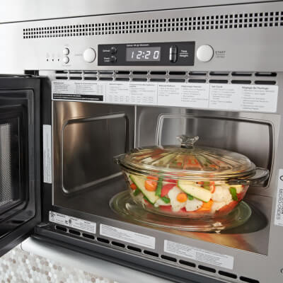Open over-the-range microwave with a bowl of vegetables inside