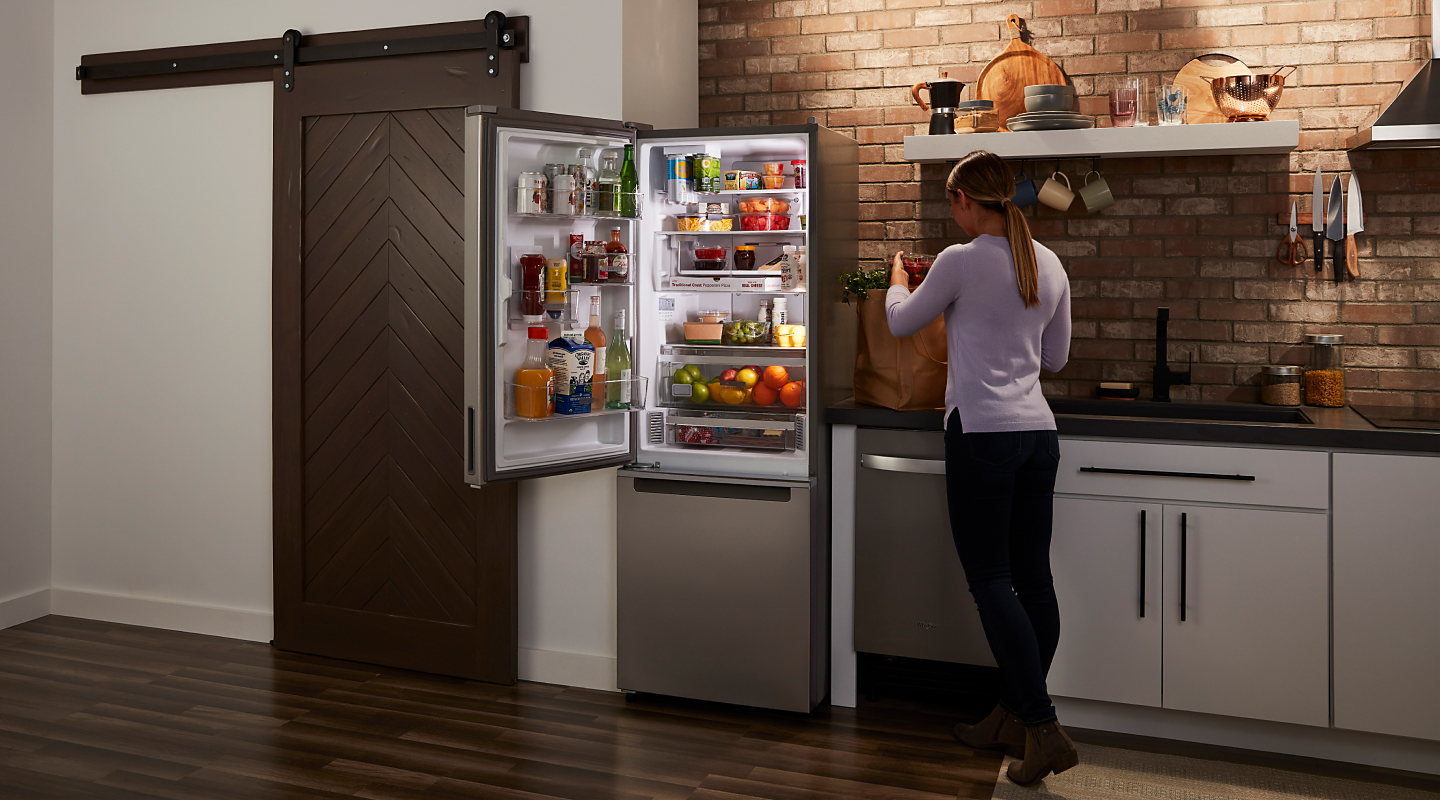 厨房里一个女人站在一个敞开的冰箱旁，冰箱里放着食物
