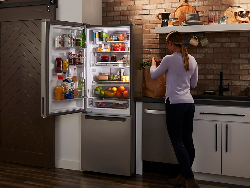 Woman standing in front of an open stainless steel Whirlpool® bottom freezer fridge