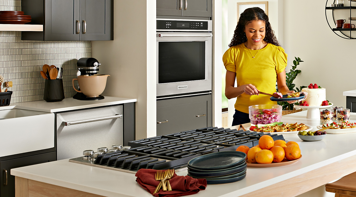 Woman making a plate next to a Whirlpool® gas cooktop
