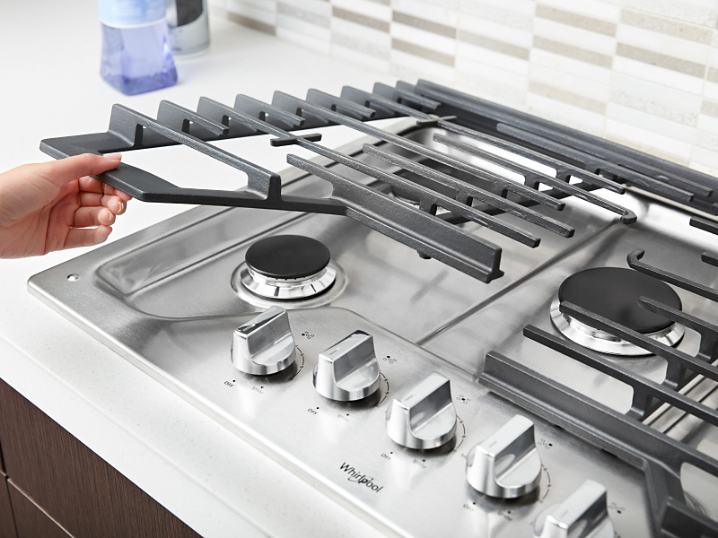 Person lifting the grate on a gas cooktop