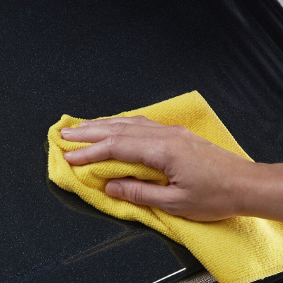 Person cleaning a cooktop with a yellow dish rag