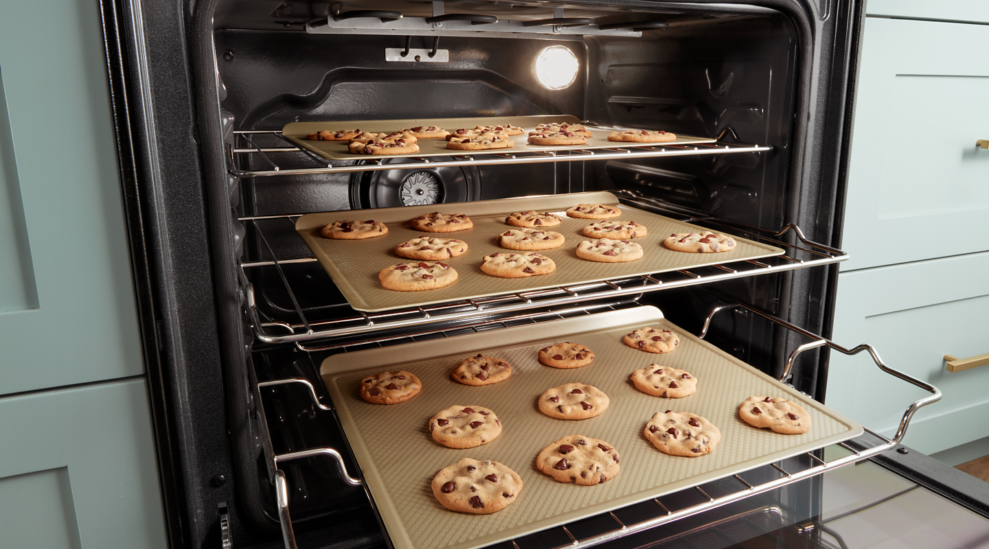 Three trays of cookies inside an oven