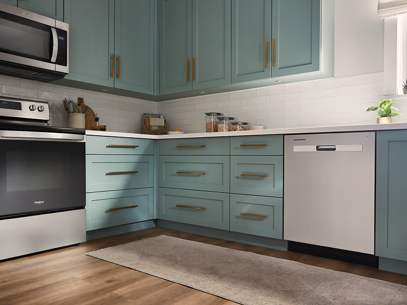 A Whirlpool® dishwasher and range in a modern kitchen with teal cabinets.