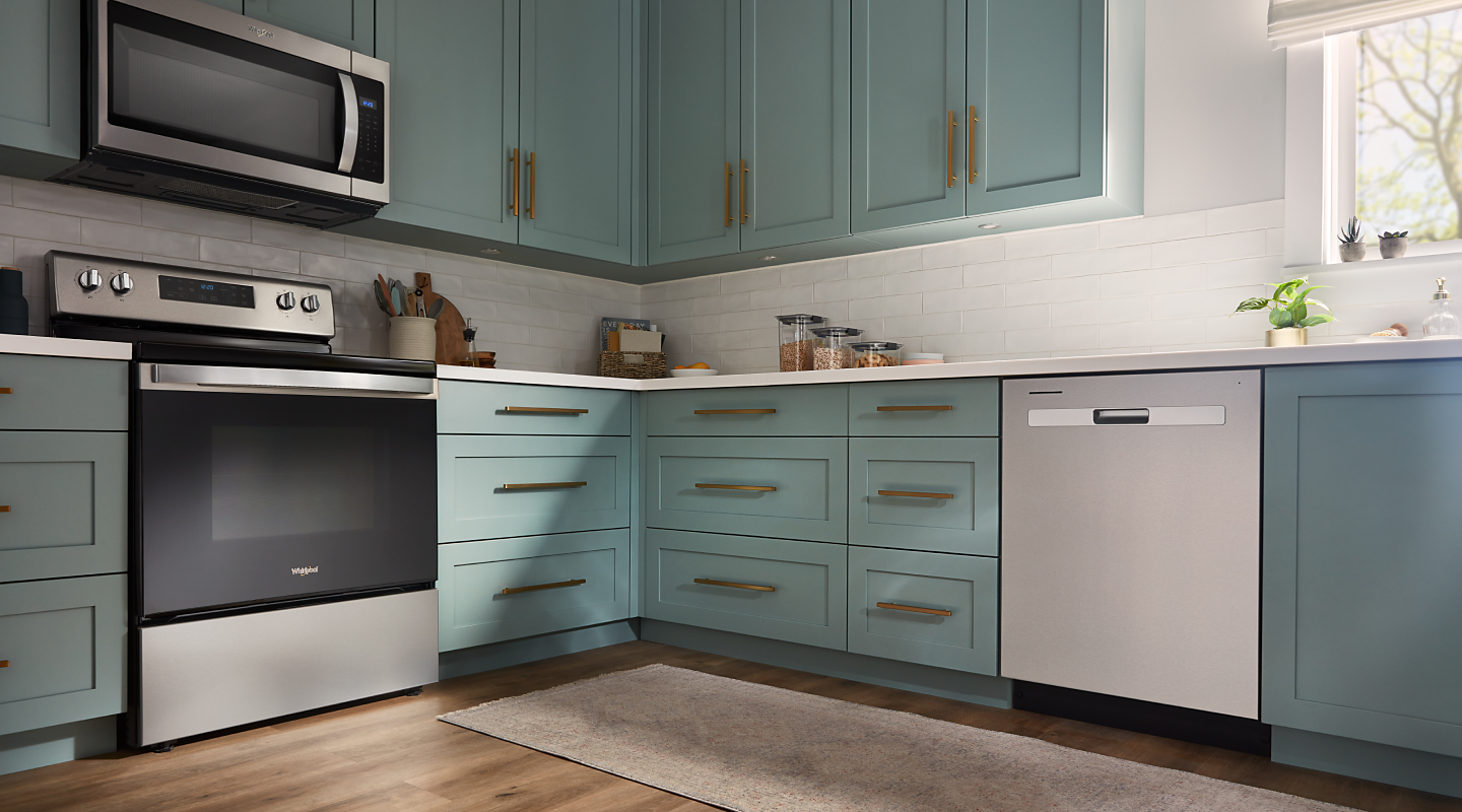 A Whirlpool® dishwasher and range in a modern kitchen with teal cabinets.