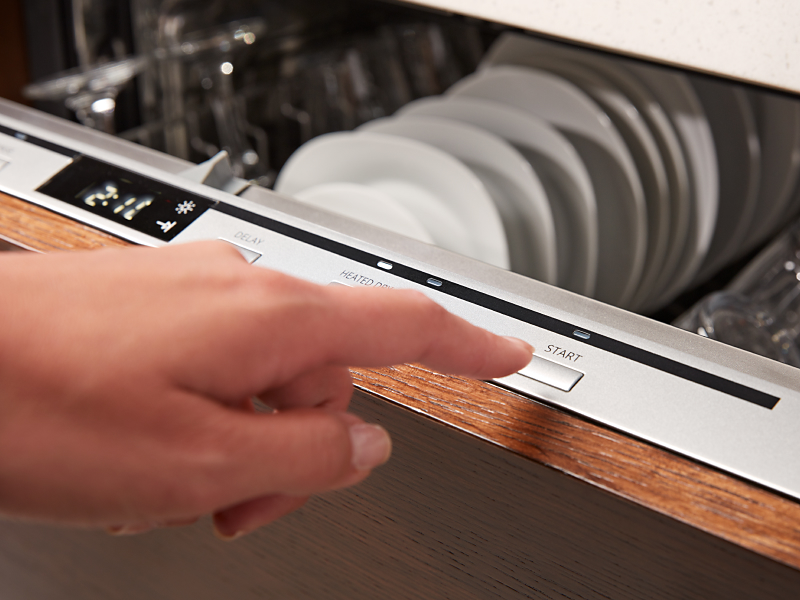 A person starting a dishwasher cycle on a top control panel.
