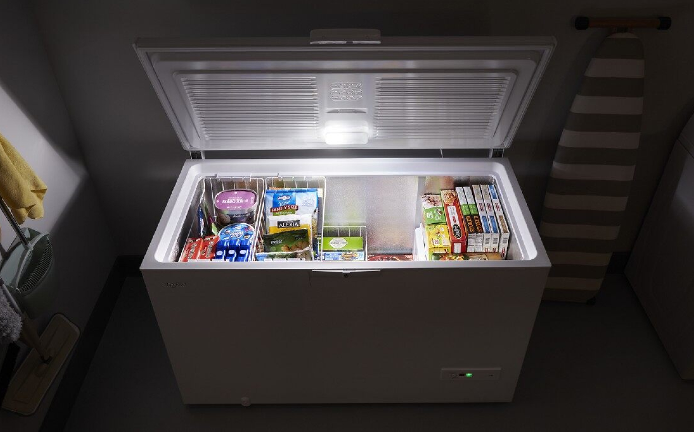 Whirlpool® deep freezer shown in dark room with lid open and LED light illuminating frozen food