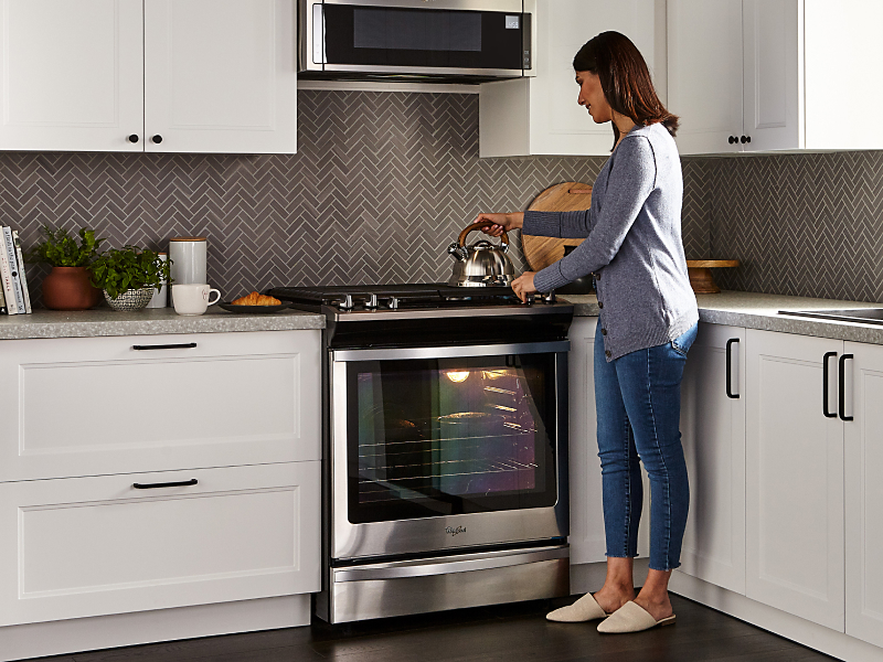 Person placing tea kettle on a gas range stovetop Person placing tea kettle on a gas range stovetop
