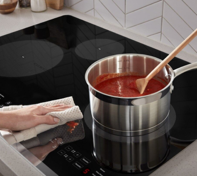 A hand wiping up sauce spilled on a Whirlpool® Induction Cooktop