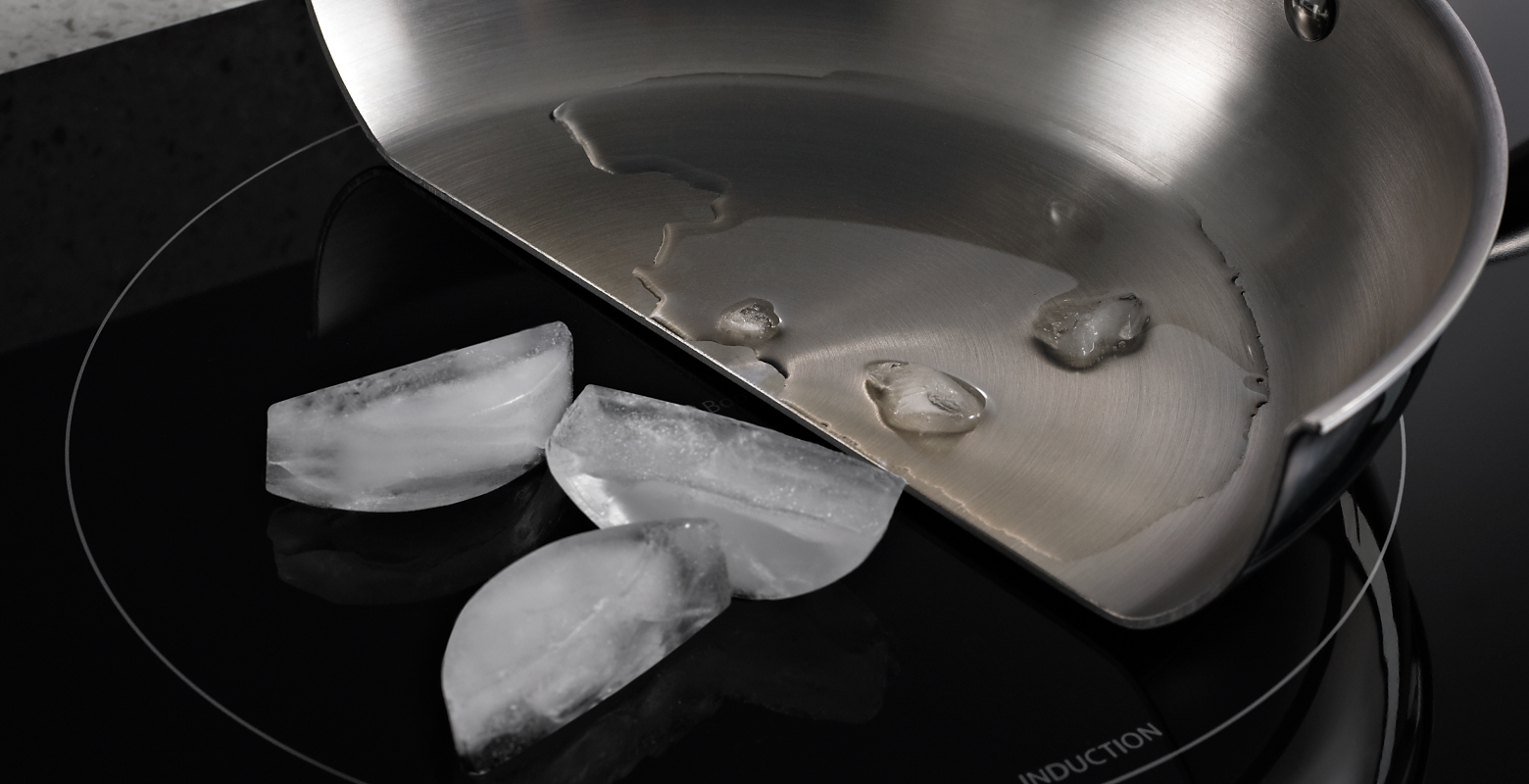 Pan cut in half with melted ice in the pan and whole ice cubes on the induction cooktop surface