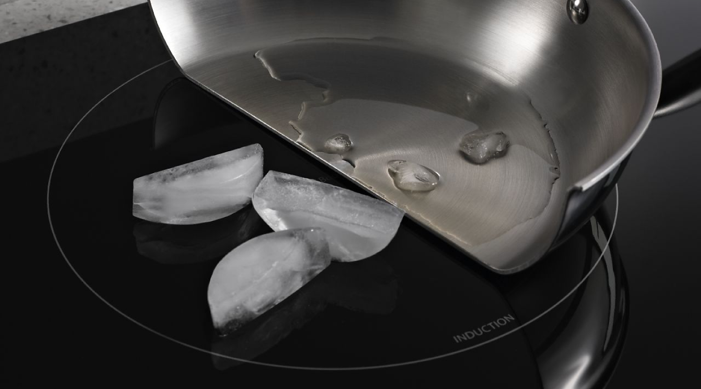 平底锅切成两半，融化的冰在锅里，整个冰块在感应灶台表面
