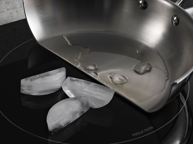 Pan cut in half with melted ice in the pan and whole ice cubes on the induction cooktop surface