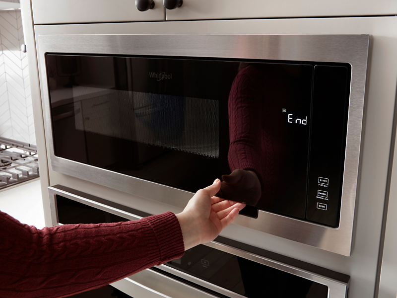 A hand opening a Whirlpool microwave