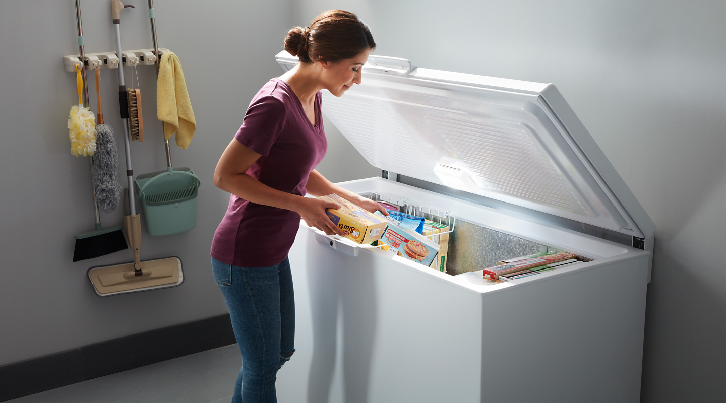 A woman placing frozen groceries into a white chest freezer