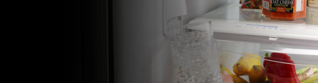 A woman fills up a water bottle from a refrigerator water dispenser.