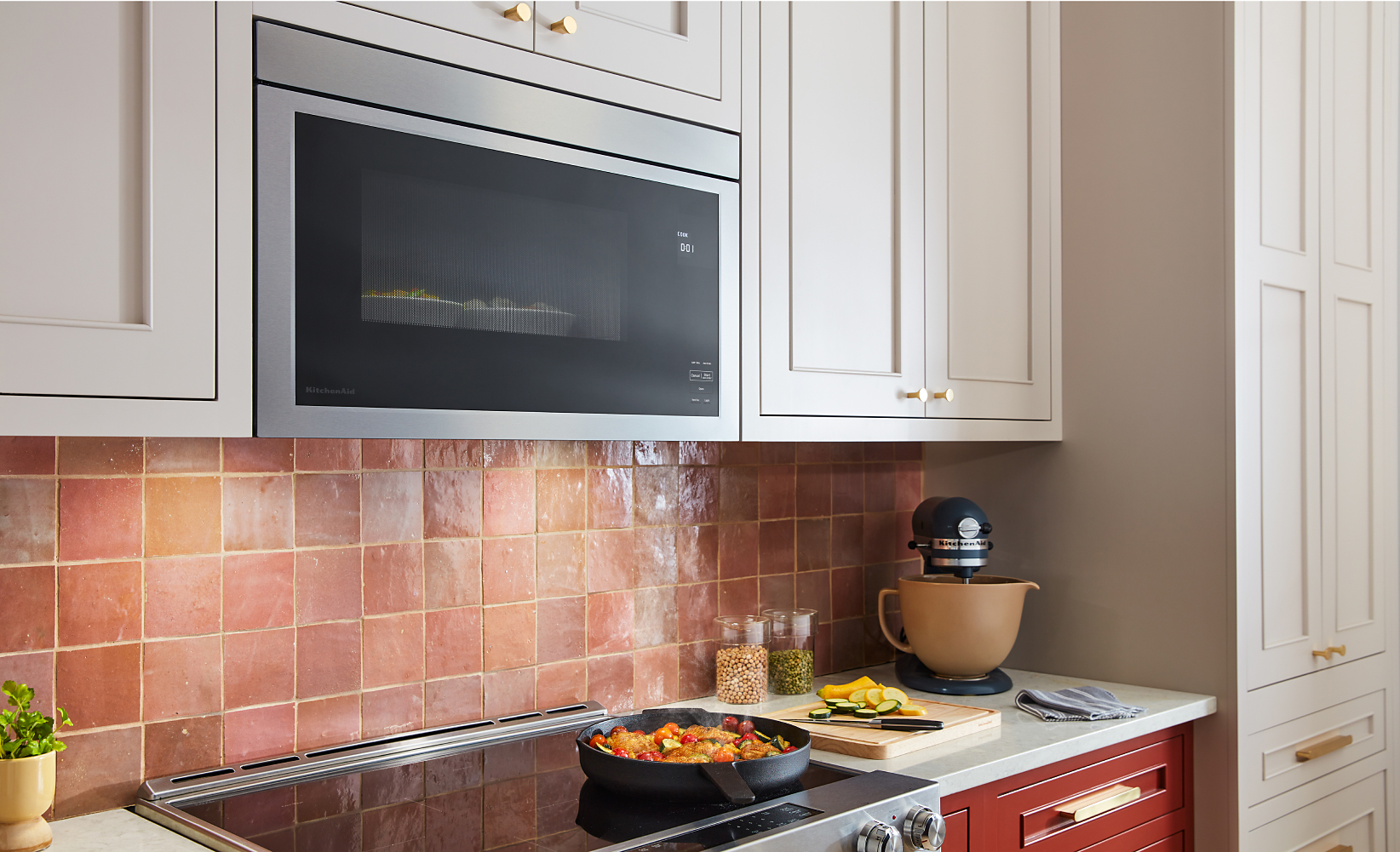 A flush built-in over-the-range microwave installed in cream cabinetry above a radiant electric cooktop with a frying pan of cooking veggies.
