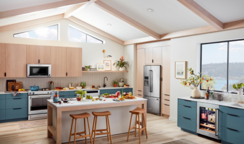 An airy, light kitchen with an island and blue-green cabinets and stainless steel appliances.