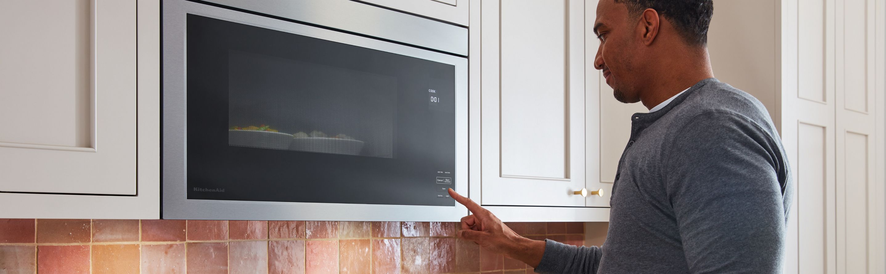 A person touching a button on KitchenAid® microwave.
